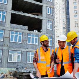 Equipo con cascos revisando planos frente a un edificio