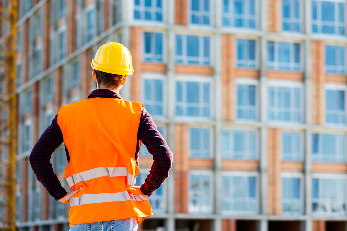 Trabajador con casco y chaleco frente a un edificio, mantenimiento de fachadas de edificios